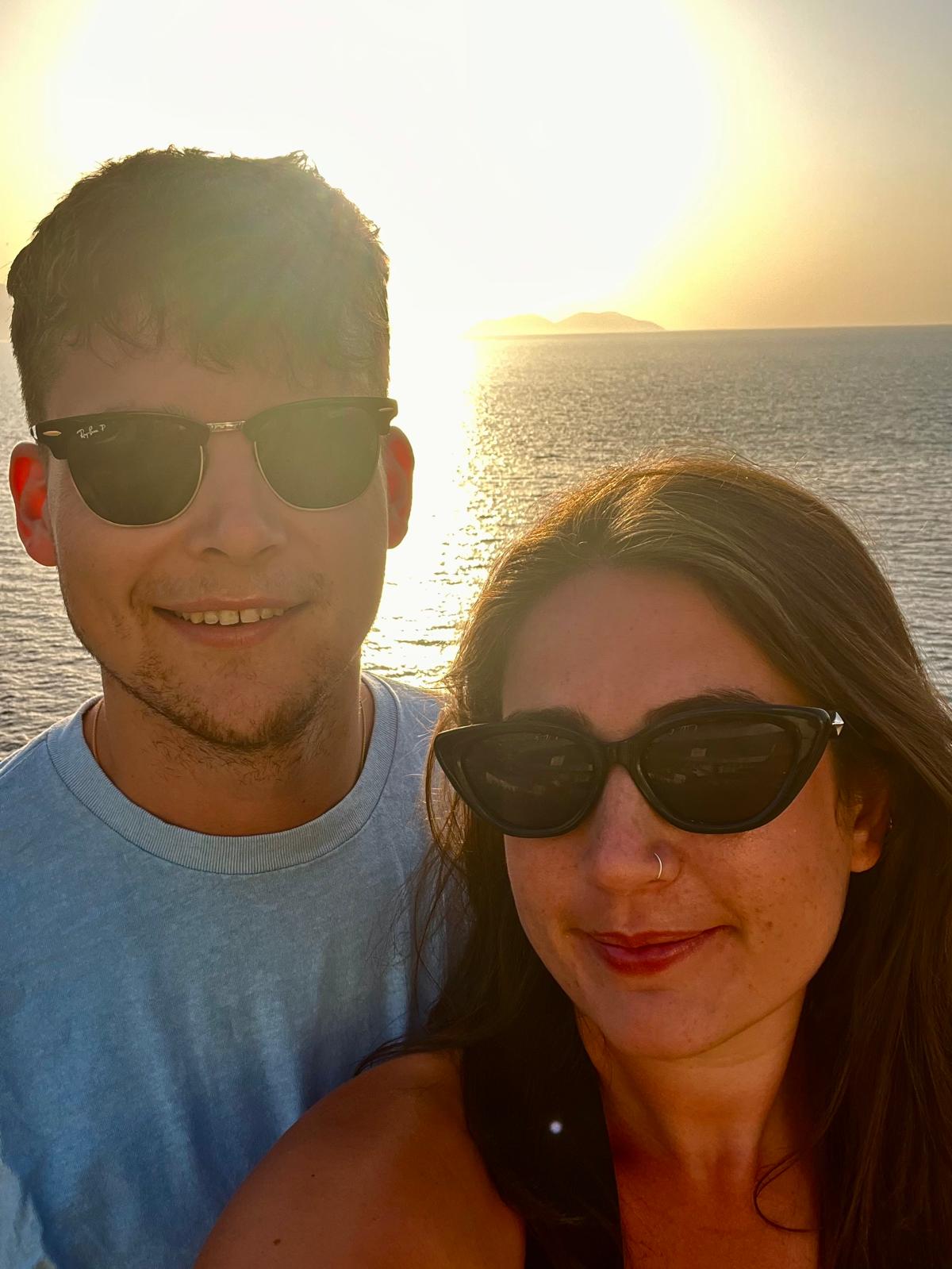 A man and a woman both wearing sunglasses standing in front of a sunset